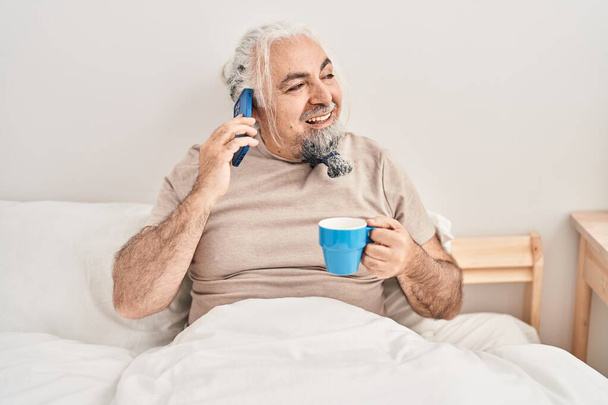 Moyen Age homme aux cheveux gris parler sur smartphone boire du café dans la chambre - Photo, image