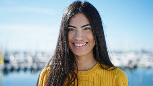 Молодая красивая латиноамериканка, уверенно улыбающаяся стоя на берегу моря - Фото, изображение