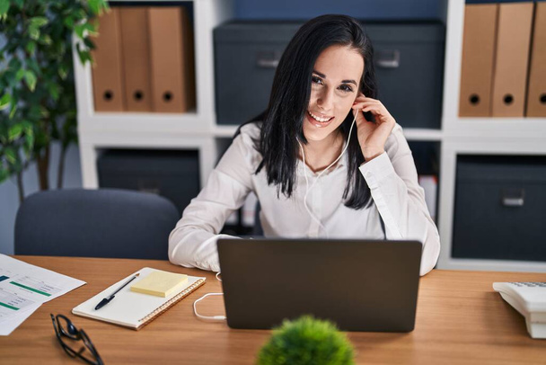 Jonge blanke vrouw zakenman met behulp van laptop en oortelefoons werken op kantoor - Foto, afbeelding