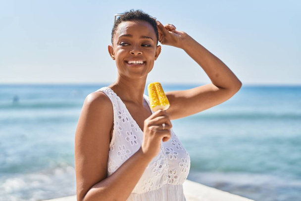 Afroamerikanerin lächelt selbstbewusst und isst Eis am Meer - Foto, Bild
