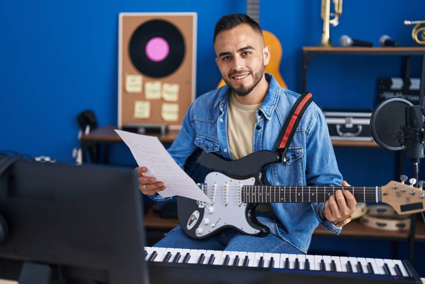 Fiatal spanyol férfi zenész játszik elektromos gitár olvasás zenei lap a zenei stúdióban - Fotó, kép