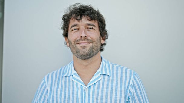 Молодий іспаномовний чоловік посміхається впевнено стоїть над ізольованим білим тлом
 - Фото, зображення