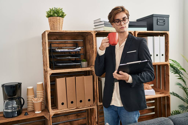 Молодий кавказький чоловік бізнесмен п'є каву, тримаючи кишеню в офісі
 - Фото, зображення
