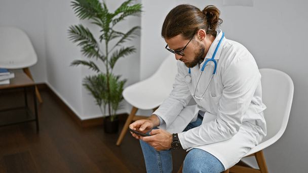 Young hispanic man doctor using smartphone working at clinic waiting room - Photo, Image