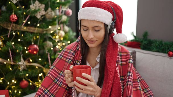 Młoda piękna Latynoska słuchająca muzyki pijąca kawę świętująca święta Bożego Narodzenia w domu - Zdjęcie, obraz