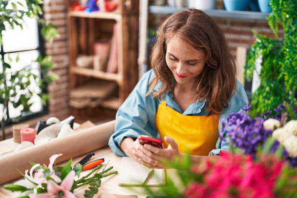 Jovem bela mulher hispânica florista sorrindo confiante usando smartphone na florista - Foto, Imagem