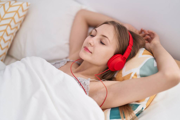 Joven mujer caucásica escuchando música relajada en la cama en el dormitorio - Foto, Imagen