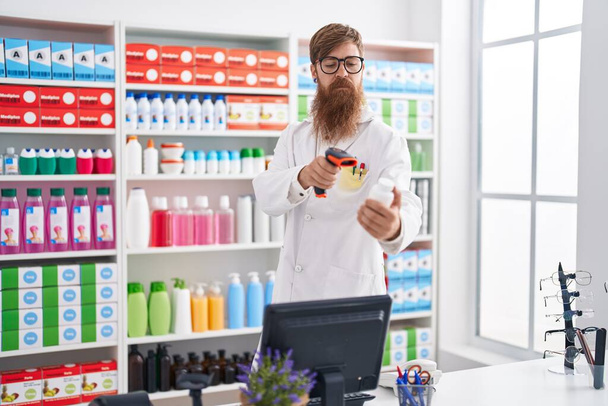 Young redhead man pharmacist scanning pills bottle at pharmacy - Photo, Image