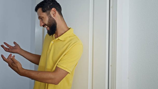 Young hispanic man opening door doing come gesture at home - Photo, Image