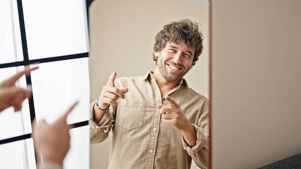 Nuori latino mies katselee peiliin osoittaa sormella kotona - Valokuva, kuva