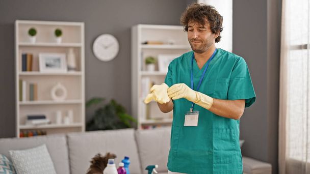 Fiatal spanyol férfi profi takarító kesztyűt visel mosolyogva otthon - Fotó, kép