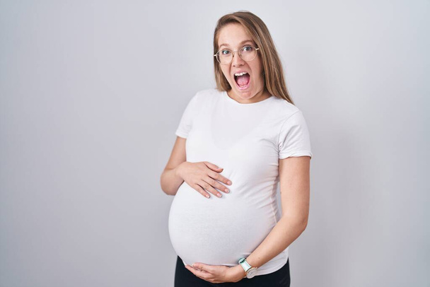 Jonge zwangere vrouw verwacht een baby, aanraken van zwangere buik vieren gek en verbaasd voor succes met open ogen schreeuwen opgewonden.  - Foto, afbeelding