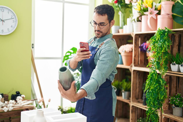 Молодой латиноамериканец флорист делает фото, чтобы посадить горшок на смартфоне в цветочном магазине - Фото, изображение