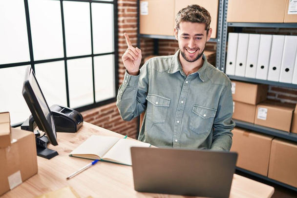 Spaanse man met baard werkt bij kleine bedrijven e-commerce glimlachend vrolijk wijzend met hand en vinger naar de zijkant  - Foto, afbeelding
