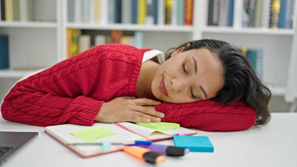 Jonge mooie Spaanse vrouw student slapen op het bureau in de bibliotheek universiteit - Foto, afbeelding
