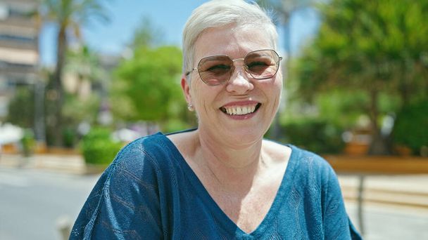Donna dai capelli grigi di mezza età con gli occhiali da sole che sorride al parco - Foto, immagini
