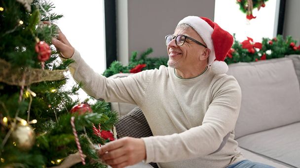 Orta yaşlı, kır saçlı adam evde Noel ağacı süslüyor. - Fotoğraf, Görsel