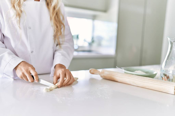 Young woman wearing cook uniform cutting dough at kitchen - Foto, Imagen