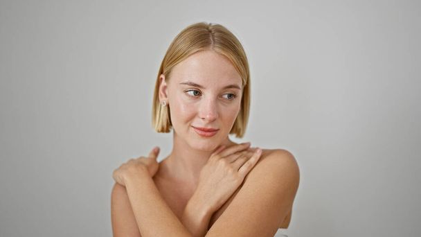 Jeune femme blonde souriant confiant toucher le cou sur fond blanc isolé - Photo, image