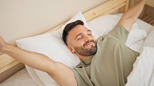 Молодий іспаномовний чоловік прокидається розтягуючи руки в спальні
 - Фото, зображення