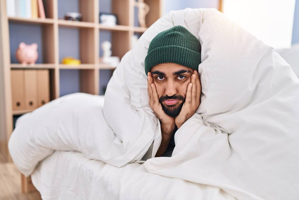 Giovane uomo ispanico sdraiato sul letto che copre con lenzuolo in camera da letto - Foto, immagini