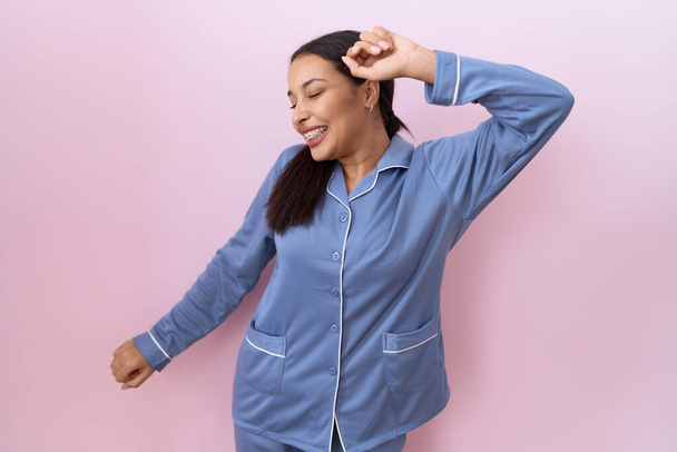 Junge Araberin in blauem Pyjama tanzt fröhlich und fröhlich, lächelt und bewegt sich lässig und selbstbewusst und hört Musik  - Foto, Bild