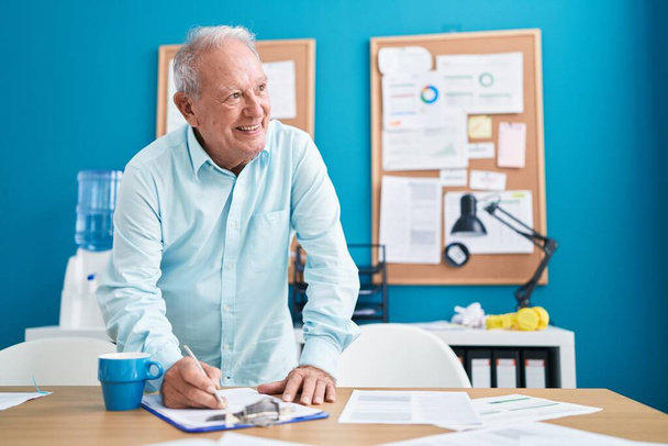 Седовласый бизнесмен среднего возраста пишет на документе в офисе - Фото, изображение