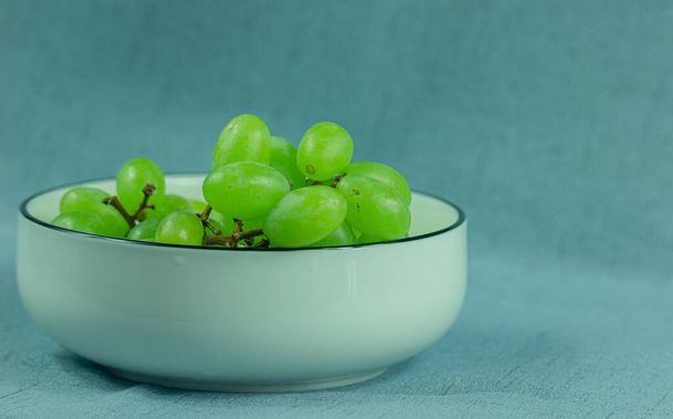 Fresh green grapes in a white ceramic bowl against a solid color background. Summer and fall fruits with a delicious taste. - Photo, Image