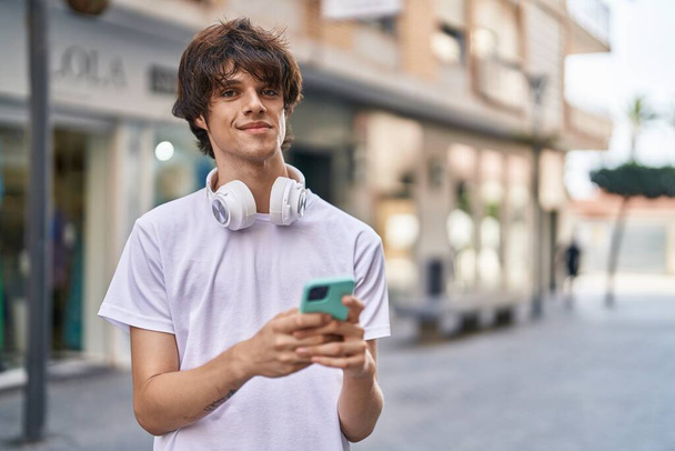 Nuori vaalea mies hymyilee luottavainen käyttämällä älypuhelinta kadulla - Valokuva, kuva