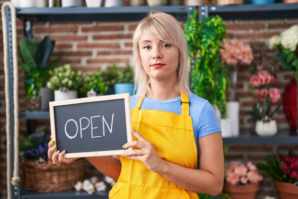 Young caucasian woman working at florist holding open sign relaxed with serious expression on face. simple and natural looking at the camera.  - 写真・画像