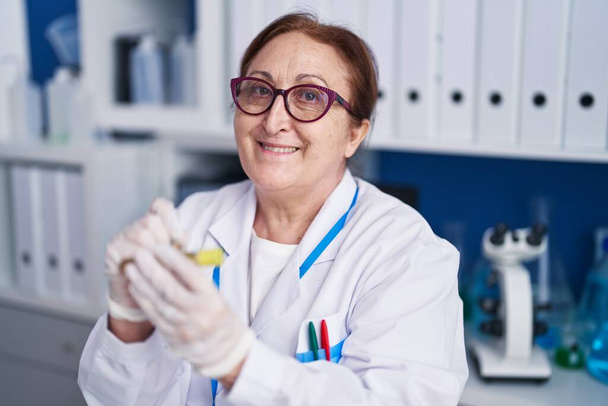 Senior vrouw wetenschapper glimlachen zelfverzekerd schrijven op reageerbuis in het laboratorium - Foto, afbeelding