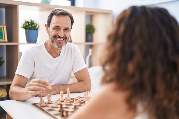 Мужчина и женщина уверенно улыбаются, играя в шахматы дома - Фото, изображение