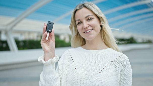 Jeune femme blonde souriante confiante tenant la clé de la nouvelle voiture au parc - Photo, image