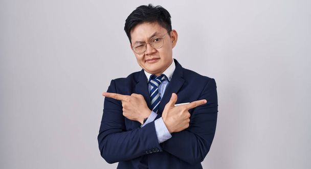 ビジネスススーツを身に着けている若いアジア人男性と指で両側を指すネクタイ,異なる方向  - 写真・画像