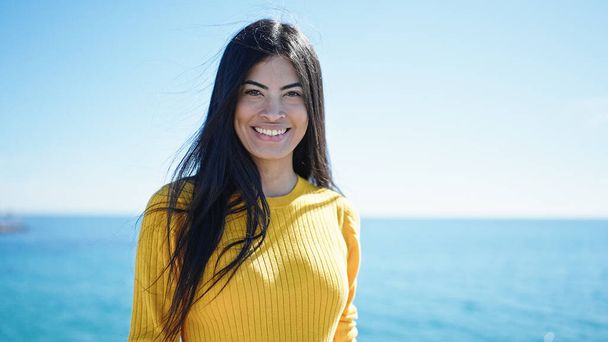 Молода красива іспаномовна жінка посміхається впевнено стоїть на узбережжі
 - Фото, зображення
