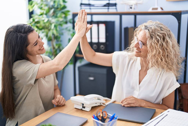 Две женщины-предпринимательницы "дай пять" с поднятыми руками в офисе - Фото, изображение