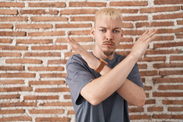 Jonge blanke man staat over bakstenen muur afwijzing uitdrukking kruising armen doen negatief teken, boos gezicht  - Foto, afbeelding