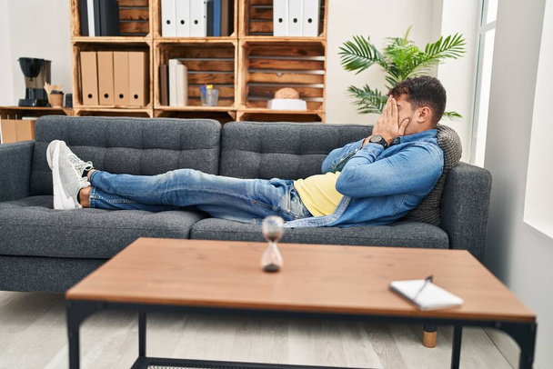 Joven paciente hispano estresado tumbado en sofá en clínica de psicología - Foto, Imagen
