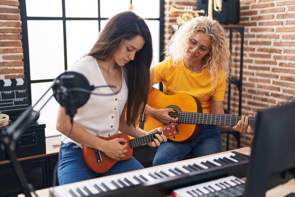 Müzik stüdyosunda klasik gitar ve ukulele çalan iki kadın müzisyen. - Fotoğraf, Görsel