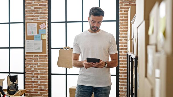 Młody latynoski człowiek e-commerce pracownik za pomocą touchpad sprawdzanie w biurze - Zdjęcie, obraz