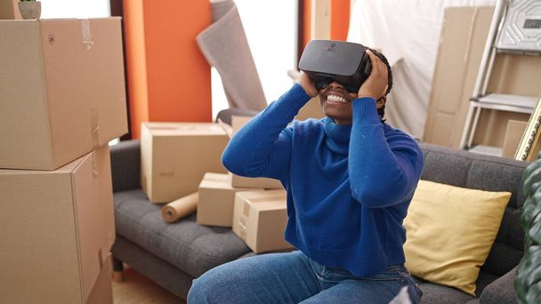 アフリカ系アメリカ人女性身に着けています仮想現実の眼鏡座っていますザソファに新しい家 - 写真・画像
