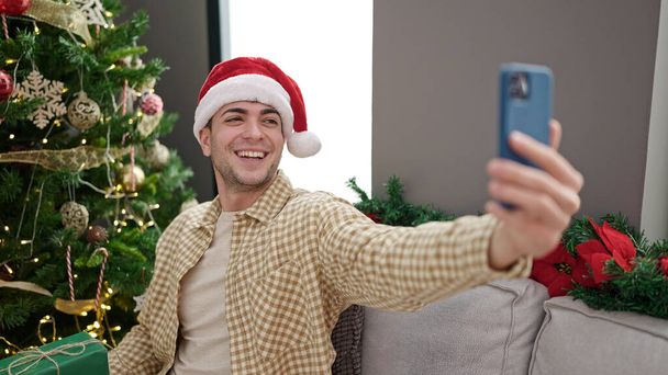 Young hispanic man taking a selfie with christmas present at home - Photo, Image