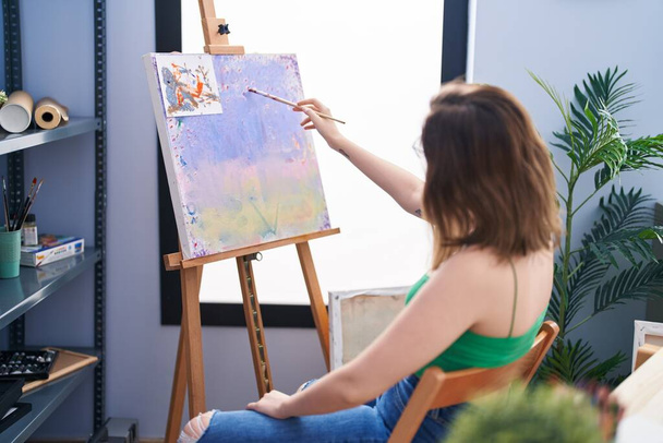 Νεαρή γυναίκα καλλιτέχνης ζωγραφίζει στο πίσω μέρος του στούντιο τέχνης - Φωτογραφία, εικόνα