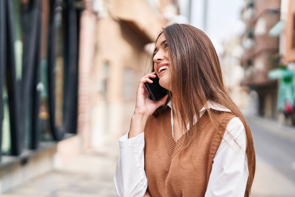 Genç, güzel, İspanyol bir kadın gülümsüyor ve caddede akıllı telefondan konuşuyor. - Fotoğraf, Görsel