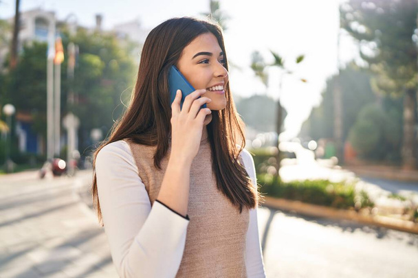 Fiatal gyönyörű spanyol nő mosolyog magabiztos beszél az okostelefonon az utcán - Fotó, kép