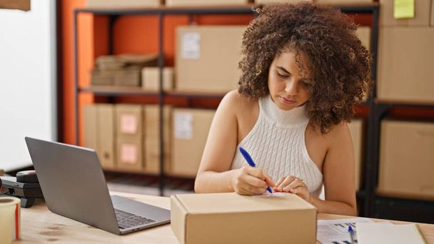 Joven mujer hispana hermosa comercio electrónico trabajador de negocios utilizando la escritura portátil en el paquete en la oficina - Foto, imagen