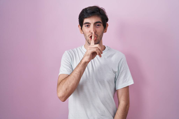Young hispanic man standing over pink background asking to be quiet with finger on lips. silence and secret concept.  - Photo, Image