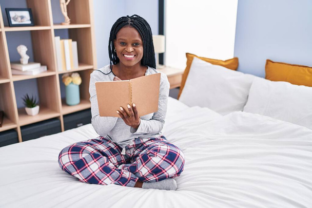 African american woman reading book sitting on bed at bedroom - Foto, immagini