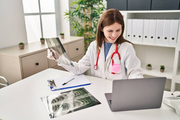 Nuori blondi nainen lääkäri etsii röntgen istuu pöydällä klinikalla - Valokuva, kuva