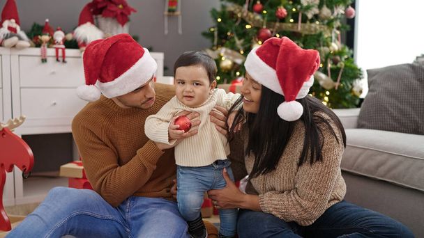 Coppia e figlio in possesso di palla decorazione seduta sul pavimento da albero di Natale a casa - Foto, immagini